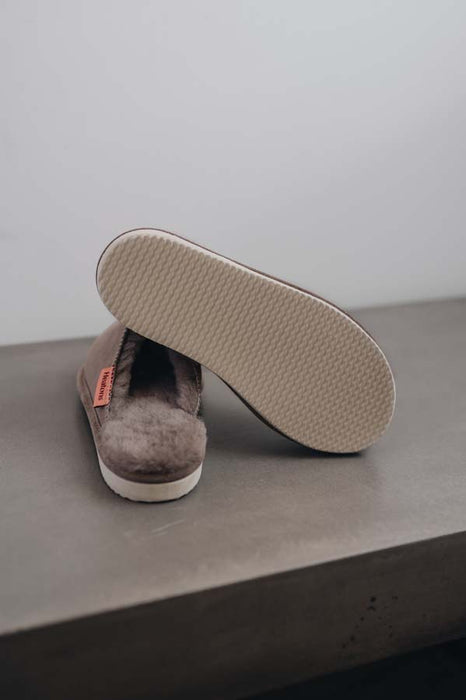 Alys Stone Sheepskin Slippers showing the bottom of the EVA sole on a Concrete Surface