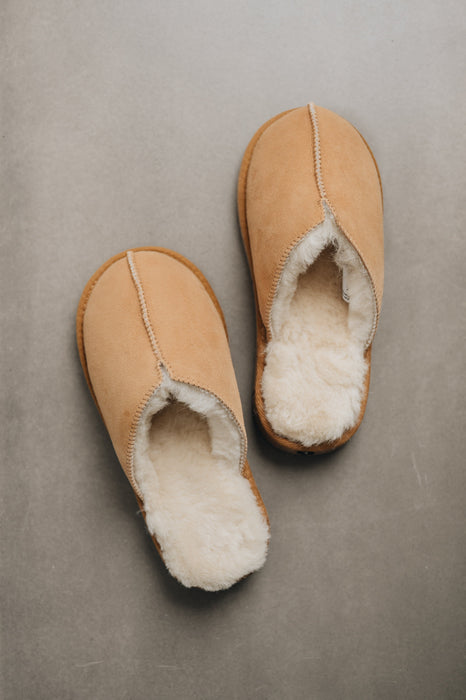 Pair of tan sheepskin slippers with white sheepskin lining on a grey background