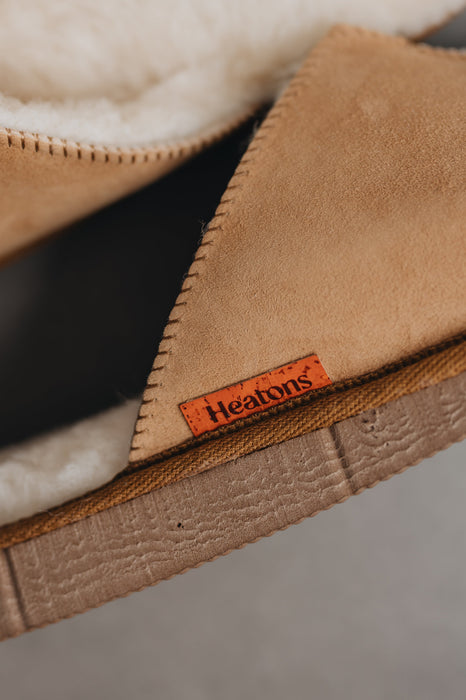 Close up of a pair of tan merino sheepskin men's mule slippers with an orange cork Heaton's label