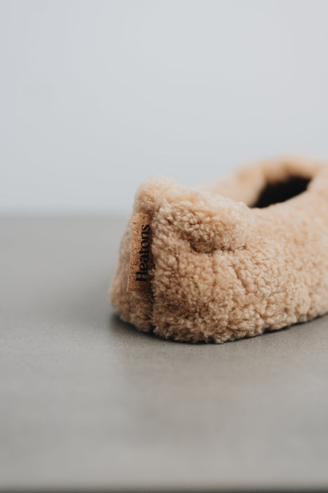 Beige curly sheepskin slipper with a cork Heatons label on a light grey stone surface 
