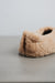 Beige curly sheepskin slipper with a cork Heatons label on a light grey stone surface 