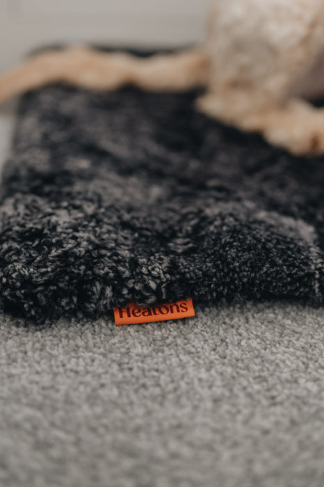Close up of a dogs leg laid on a black smoke coloured sheepskin pet bed