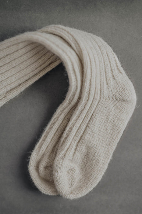 Ribbed beige natural merino wool sock on a light grey background - detail of ribbed sock and toe post