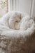 White sheepskin bean bag in a room with a window and white wall.