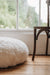 White sheepskin footstool and wooden chair on a wooden floor with a window in the background