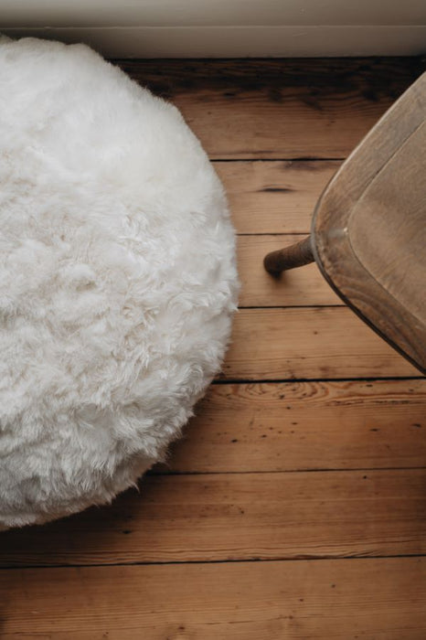 Round white sheepskin footstool on a wooden floor