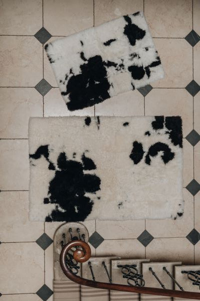 Two designer spotted sheepskin rugs with black and white pattern on a tiled floor.