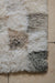 Patchwork rug of sheepskin squares in various natural melange shades on a beige floor.