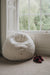 White sheepskin bean bag chair next to a window with a pair of slippers on a carpeted floor.