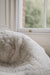 Close-up of a white sheepskin beanbag with a blurred window background.