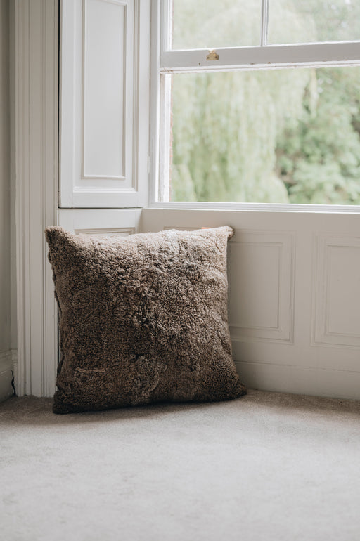 Brown sheepskin textured floor cushion in a window bay with a blurred outdoor view