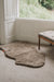 Wheat brown sheepskin rug on a carpeted floor with a window and bench in the background