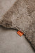 Close-up of a wheat brown sheepskin rug with an orange cotton Heatons brand tag.