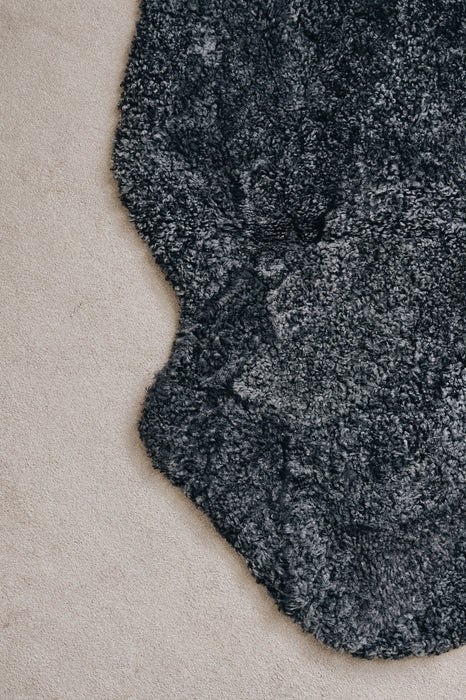 Close-up of a black smoke coloured sheepskin rug on a light coloured carpet