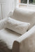 White armchair with a white sheepskin pillow in a softly lit room.
