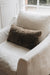 White armchair with a brown textured sheepskin cushion in a softly lit room.