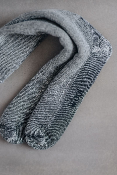Pair of grey and black merino walking socks with 'Wool' text on the sole on a grey background