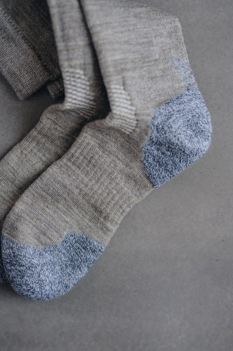 Fine knit beige merino wool socks with blue toes and cuffs on a grey background