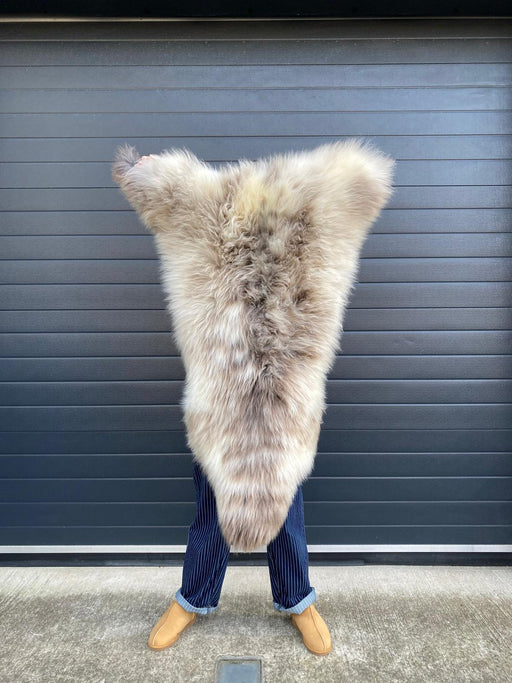 sheepskin rug being held up to show natural markings, cream with light brown dappled markings