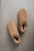 A pair of taupe sheepskin slippers with a soft shearling lining, photographed from a top-down angle on a neutral grey background.