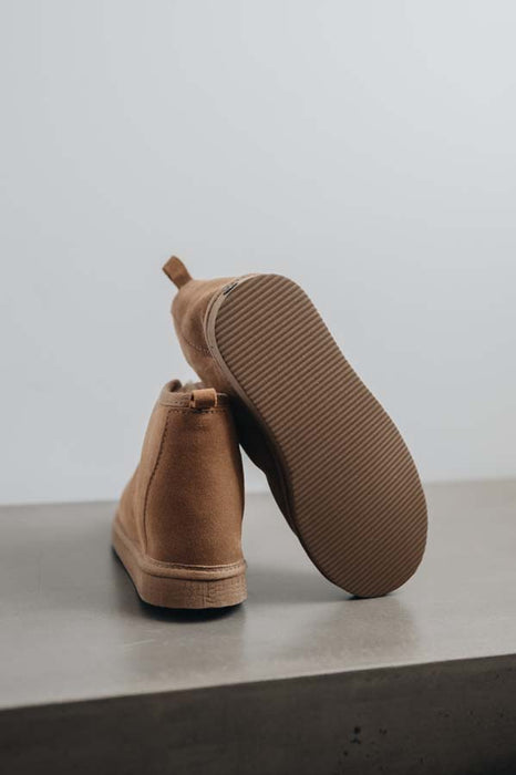 A pair of tan genuine sheepskin ankle boots, with one boot standing upright and the other leaning on its side to show the textured sole, set against a minimalist grey background.
