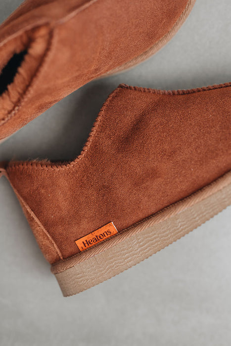 Close up of rust coloured ankle-high sheepskin slipper with orange cork label showing the Heatons brand