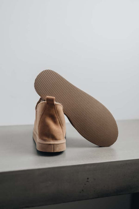 Close up of tan coloured ankle-high sheepskin slipper showing the ribbed underside of the PVA sole