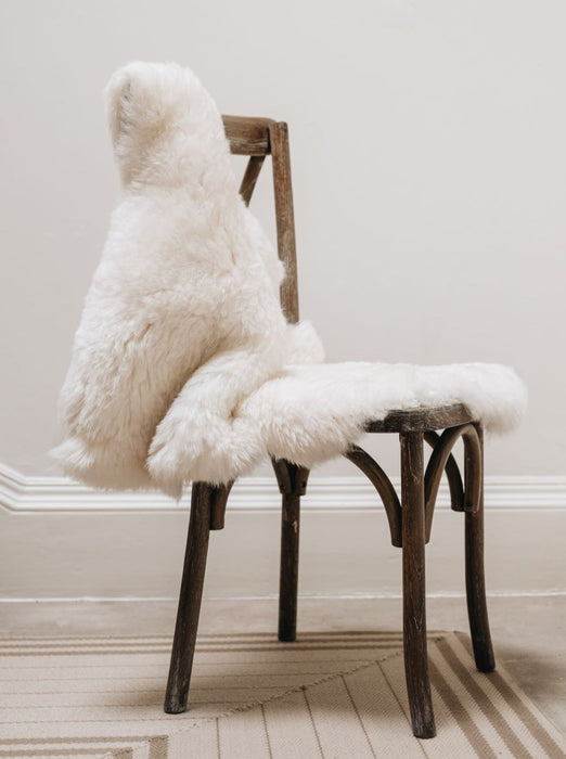 Super soft short Wool Icelandic Sheepskin Rug in white, hung over a wooden chair