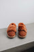 Front view of a pair of rust coloured sheepskin slippers on a light grey surface with a white background
