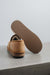 A tan men's sheepskin slipper shown from the back with its sole propped up, revealing a ribbed brown outsole