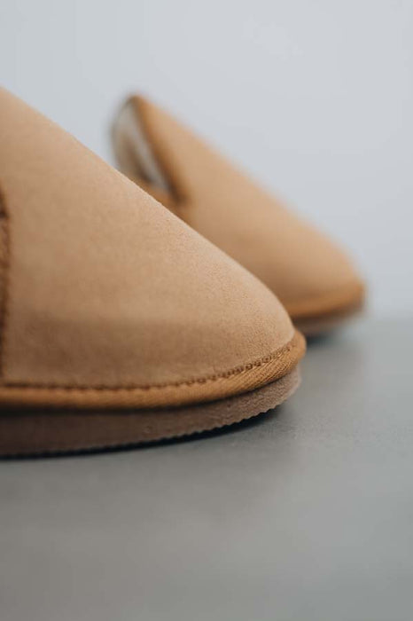 Close up of tair of tan sheepskin slippers on a light grey stone background