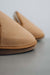 Close up of tair of tan sheepskin slippers on a light grey stone background