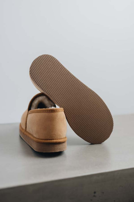 Tan sheepskin slipper with brown PVA sole on a light grey stone surface