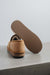 Tan sheepskin slipper with brown PVA sole on a light grey stone surface