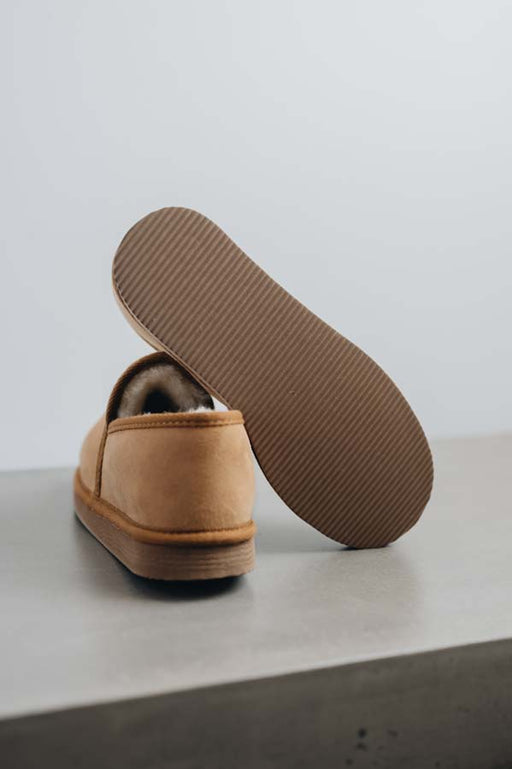 Tan sheepskin slipper with brown PVA sole on a light grey stone surface