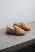 Pair of tan sheepskin slippers with shearling lining on a concrete surface.