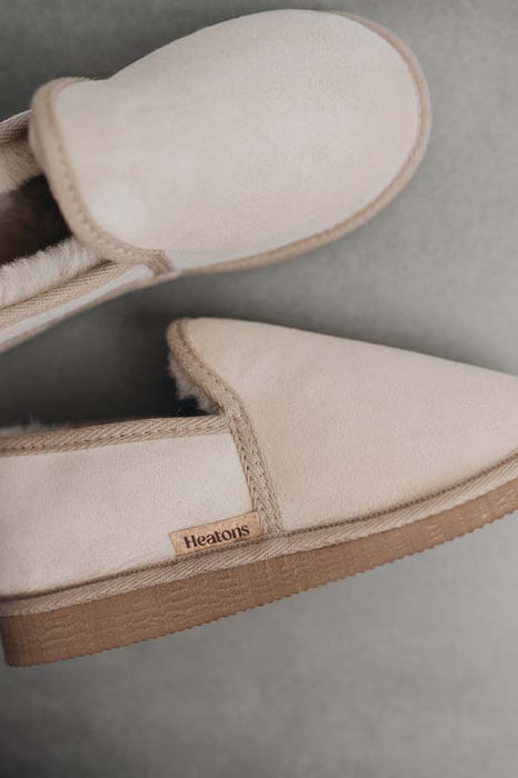 Vanilla sheepskin loafers with brown soles on a stone background