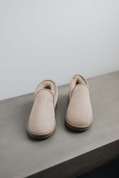 Pair of vanilla sheepskin slippers on a grey stone surface with a white background