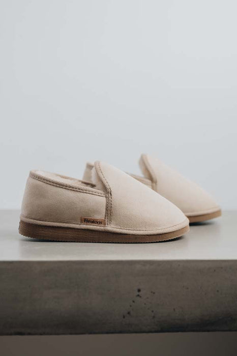 Profile view of a pair of vanilla sheepskin slippers on a concrete surface 