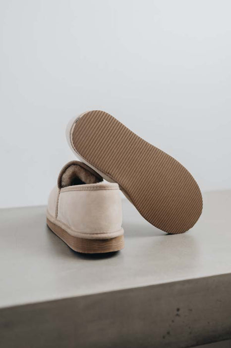 Vanilla sheepskin slipper with brown PVA sole on a light concrete surface