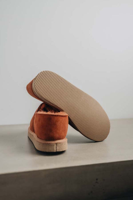 Close up of rust coloured loafer style sheepskin slipper showing the ribbed underside of the PVA sole