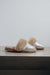 A pair of open-toe slippers with metallic silver uppers and fluffy beige genuine sheepskin trim, resting on a stone surface against a light grey background.