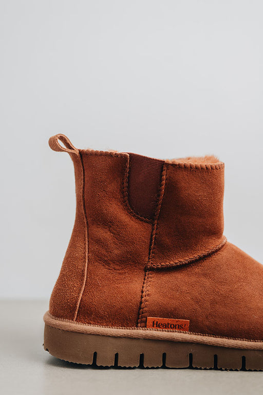 Close-up of a the back of a rust coloured sheepskin boot with 'Heatons' branding and a chunky sole.