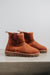 Profile view of a rust coloured sheepskin boot with 'Heatons' branding and a chunky sole.