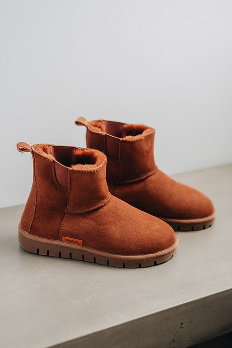 Profile view of a rust coloured sheepskin boot with orange coloured cork 'Heatons' branding and a chunky sole.
