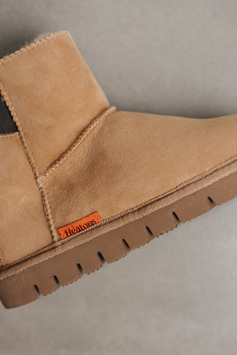 Close-up of a tan sheepskin  boot with a visible brand logo on a neutral background