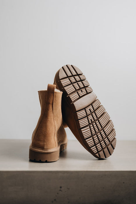 Tan sheepskin boots with a focus on the sole against a light grey stone background