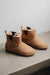 Pair of tan sheepskin chelsea style boots with dark brown elastic on a light surface.