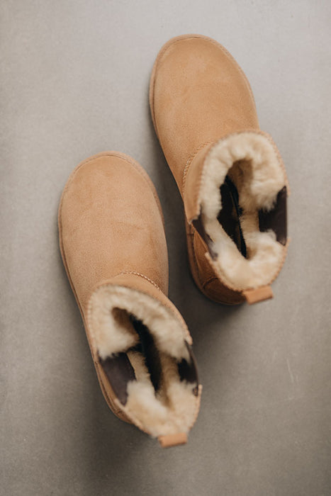 Pair of tan sheepskin boots with fur lining on a grey background