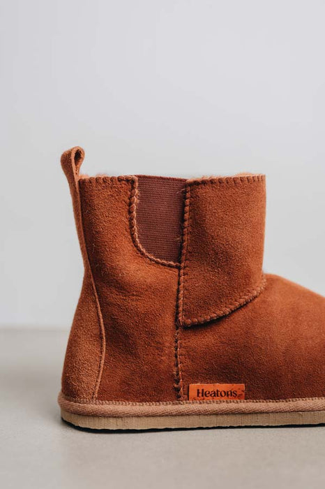 Close-up of heel of  rust coloured sheepskin boots on a light concrete background.